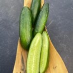 One half and three Cengelkoy cucumbers photographed in a long, wooden container, photographed on a background with marble pattern.