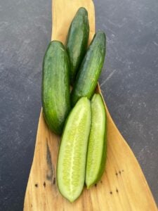 One half and three Cengelkoy cucumbers photographed in a long, wooden container, photographed on a background with marble pattern.