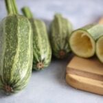 Four whole and one carved Kars Yemeklik summer squash fruits photographed on backdrop and cutting board.